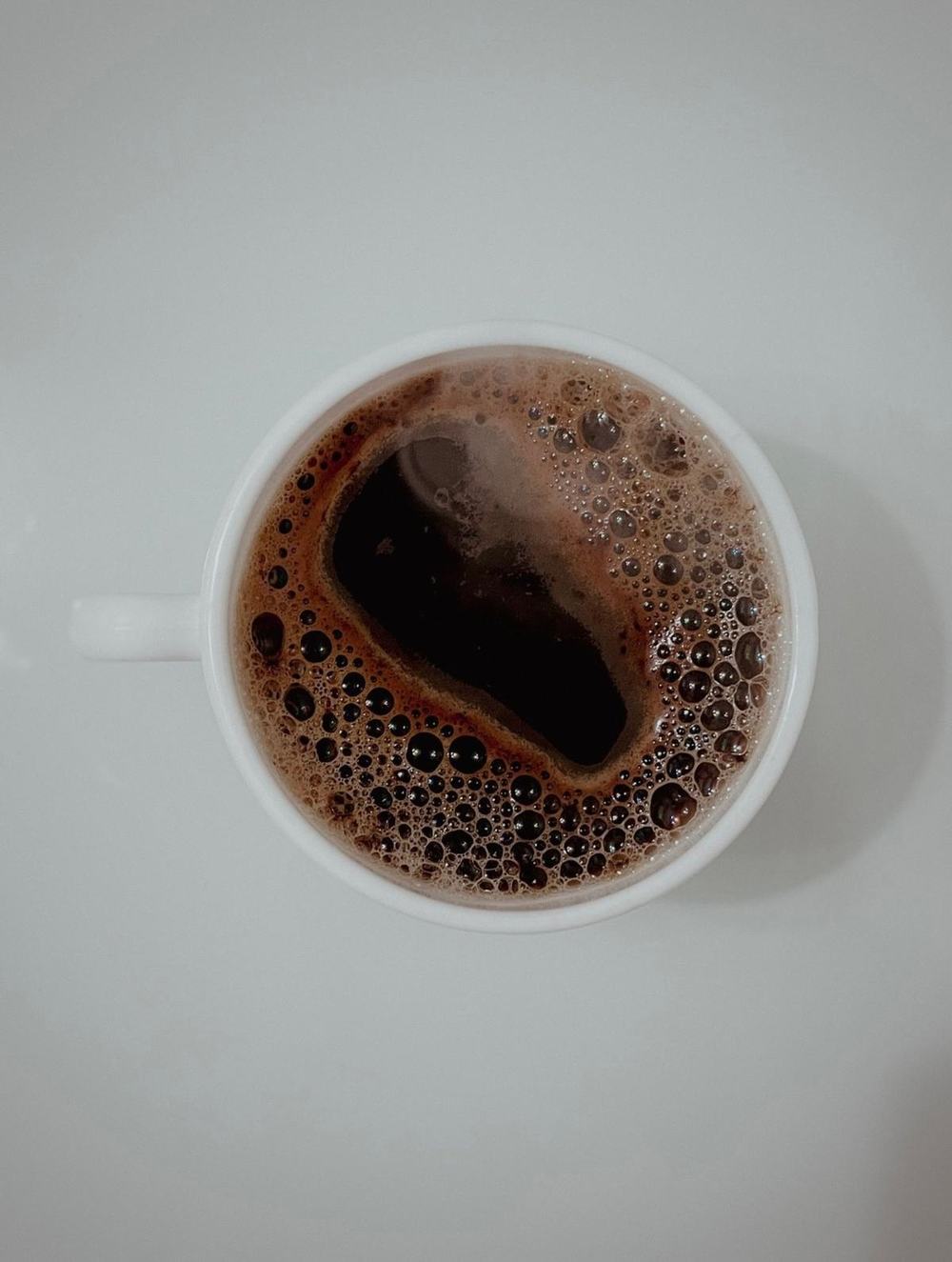 Top view of a cup of black coffee with foam on a white table