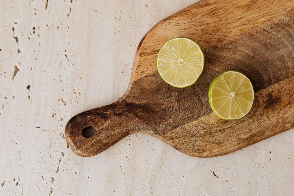 Wooden cutting board with handle and two lime halves on a cream travertine countertop