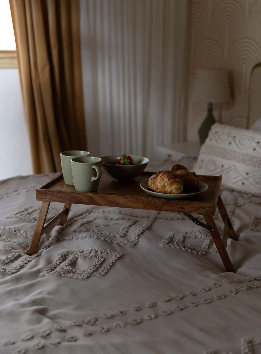 A wooden bed tray with folding legs holding two green mugs