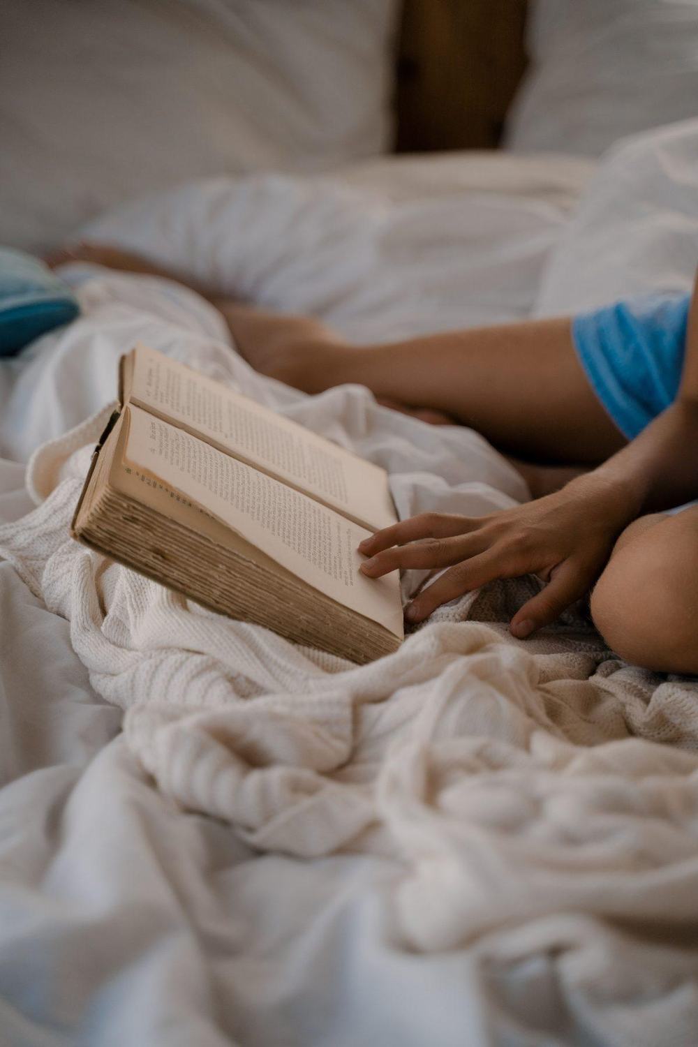 Person reading an old book in bed on a cream knit blanket