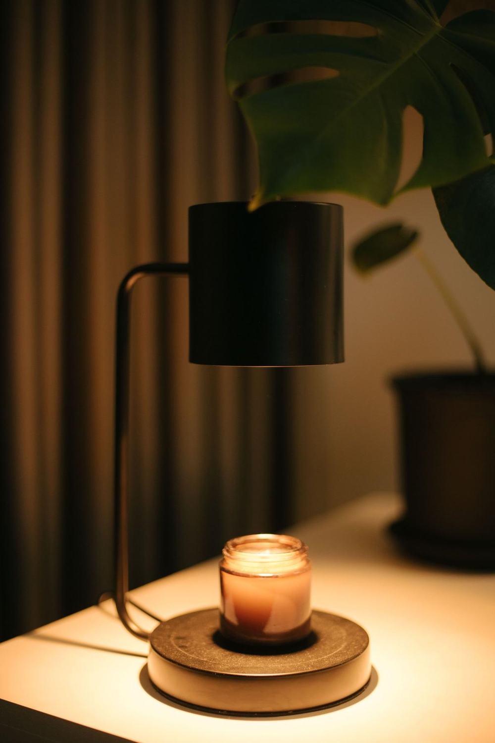 A black candle warmer lamp melting a candle in a glass jar on a table