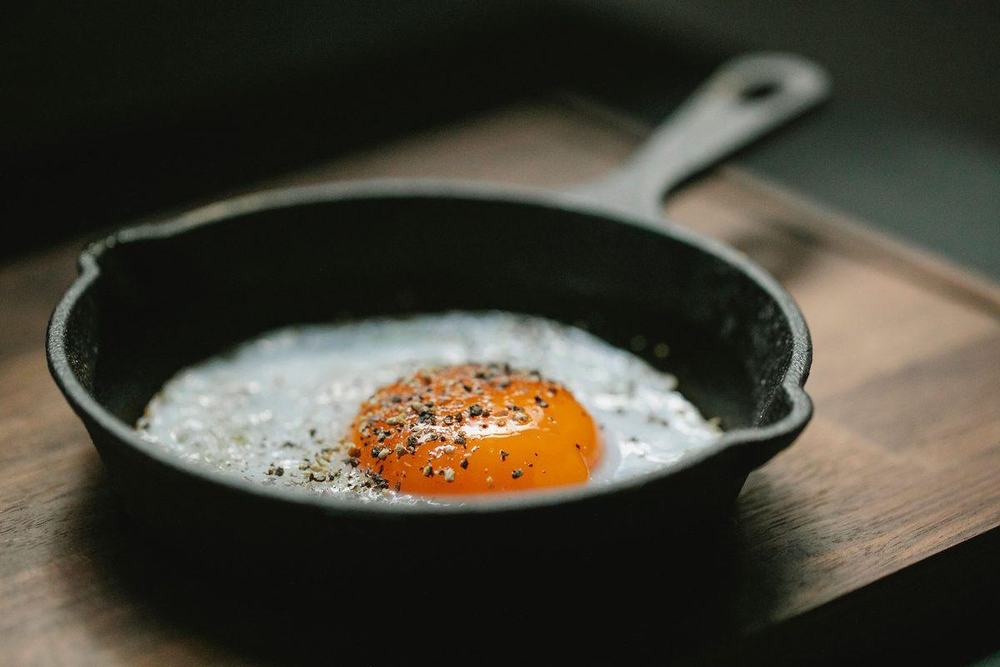 Fried egg with black pepper in a black cast iron skillet on a wooden board