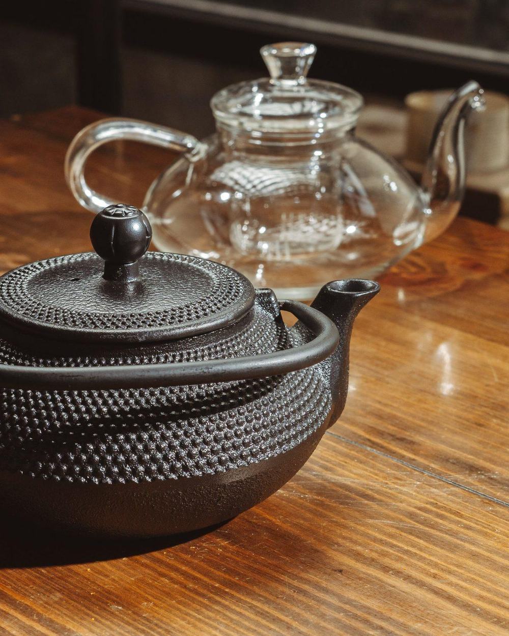 Black Japanese cast iron teapot with hobnail texture on a sunlit wooden table
