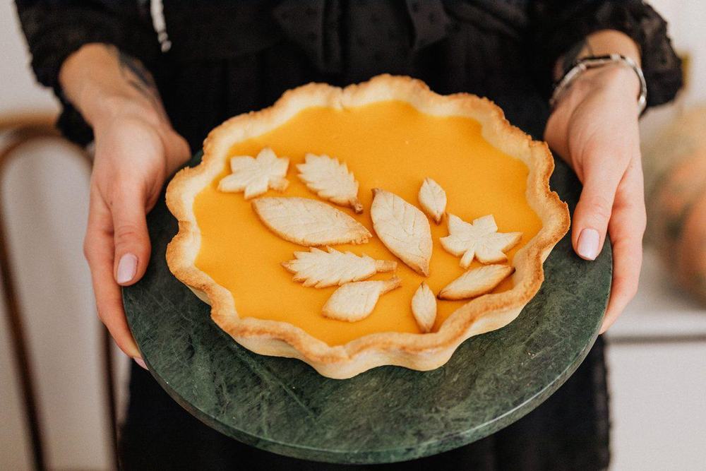 Homemade pumpkin pie with pastry leaves on a green marble board