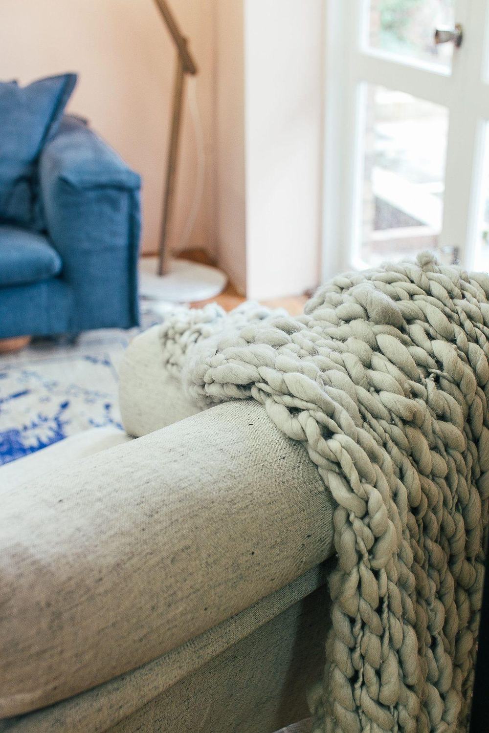 Sage green chunky knit throw blanket draped over the arm of a linen sofa