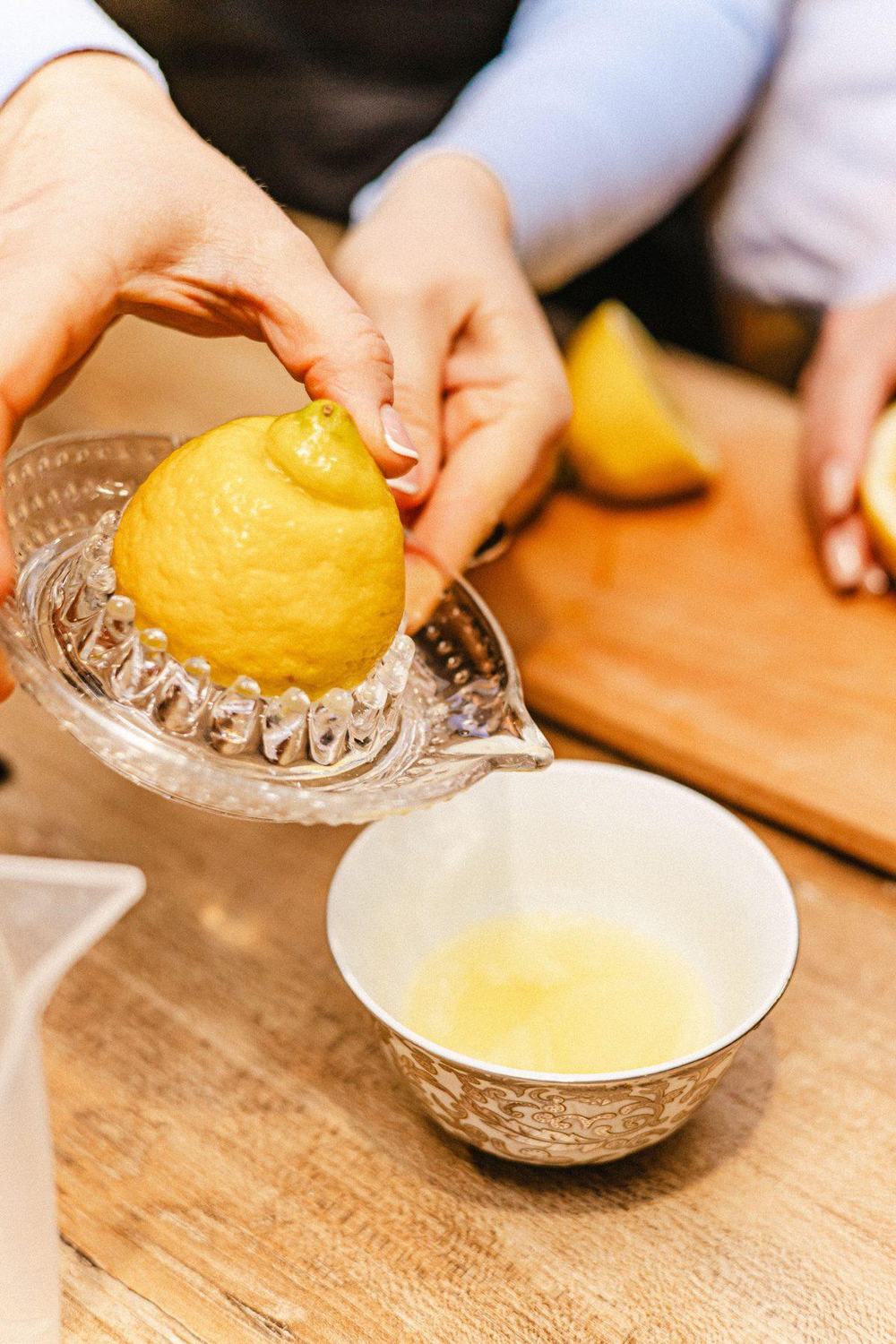 Hands squeezing a lemon on a clear glass citrus juicer over a porcelain bowl