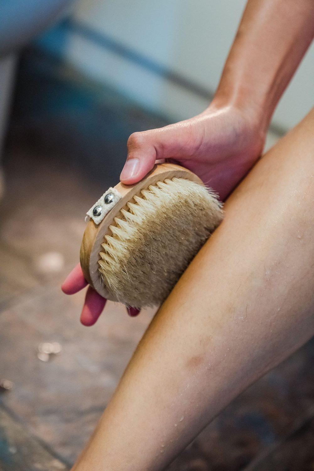 Hand holding a wooden dry body brush with natural bristles against the leg