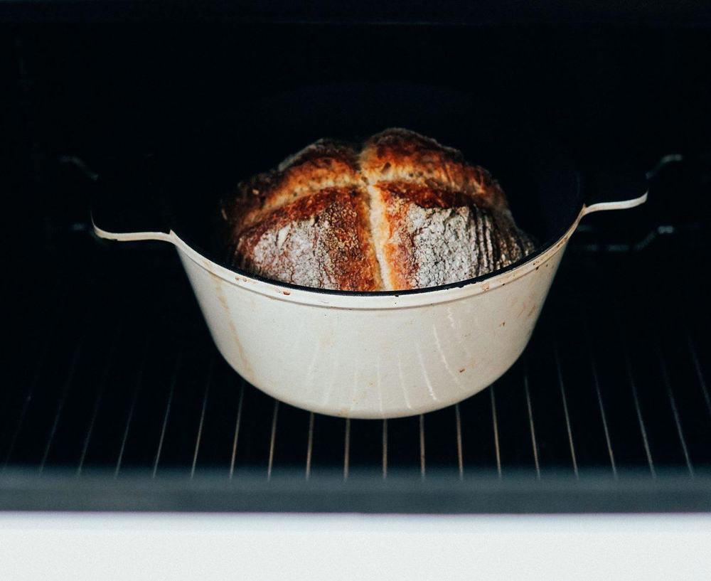 Crusty homemade bread baked in a cream enameled cast iron Dutch oven inside the oven
