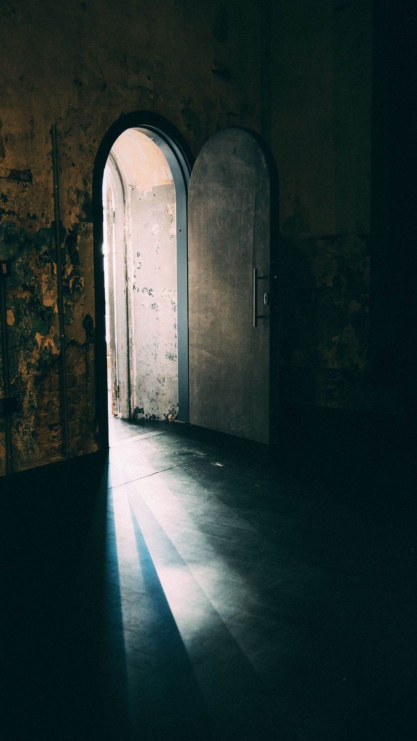 A door left slightly open in a dark old room, a strip of daylight falling across the floor