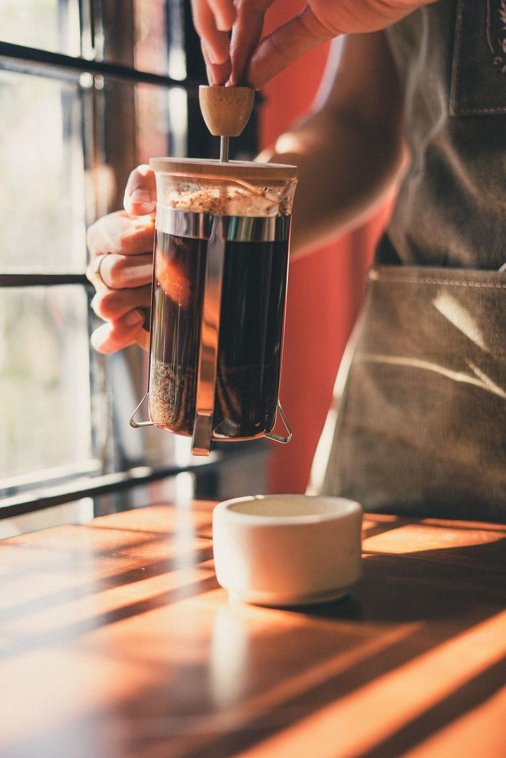 A hand pressing down a French press with a bamboo lid