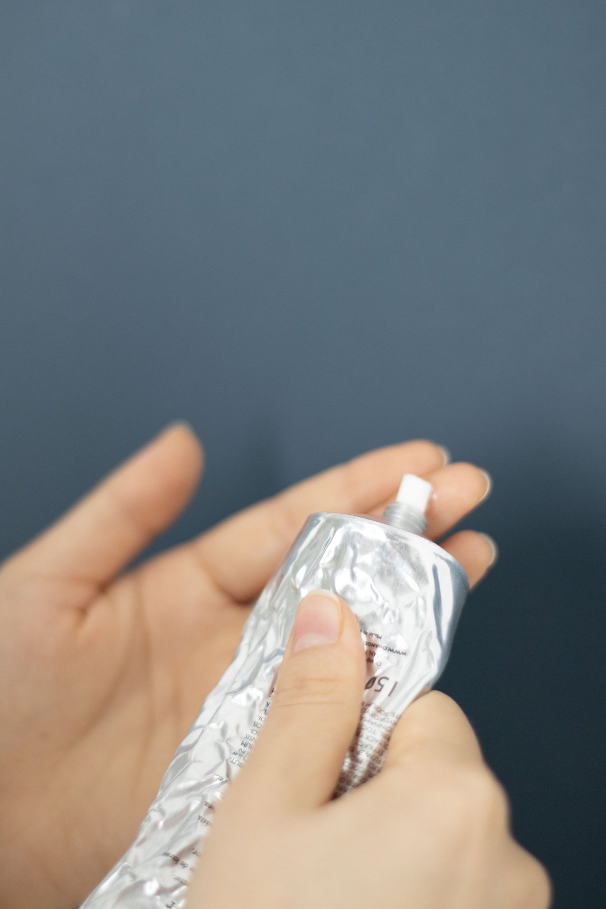 Hands squeezing a silver tube of hand cream against a dark blue background