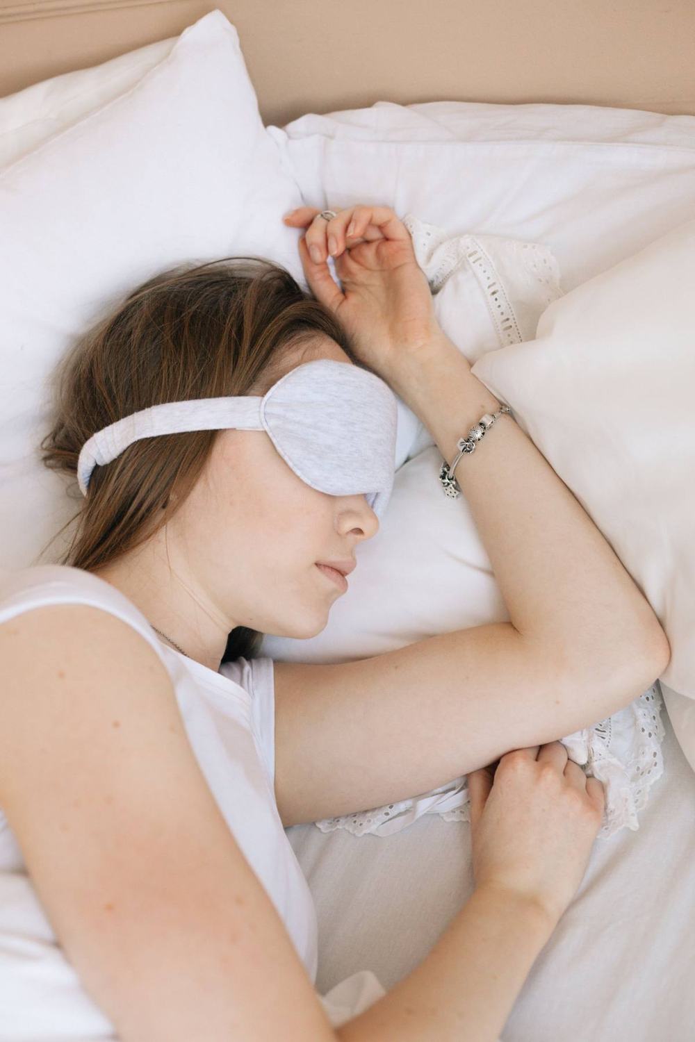 A woman sleeping on white pillows wearing a soft grey eye mask