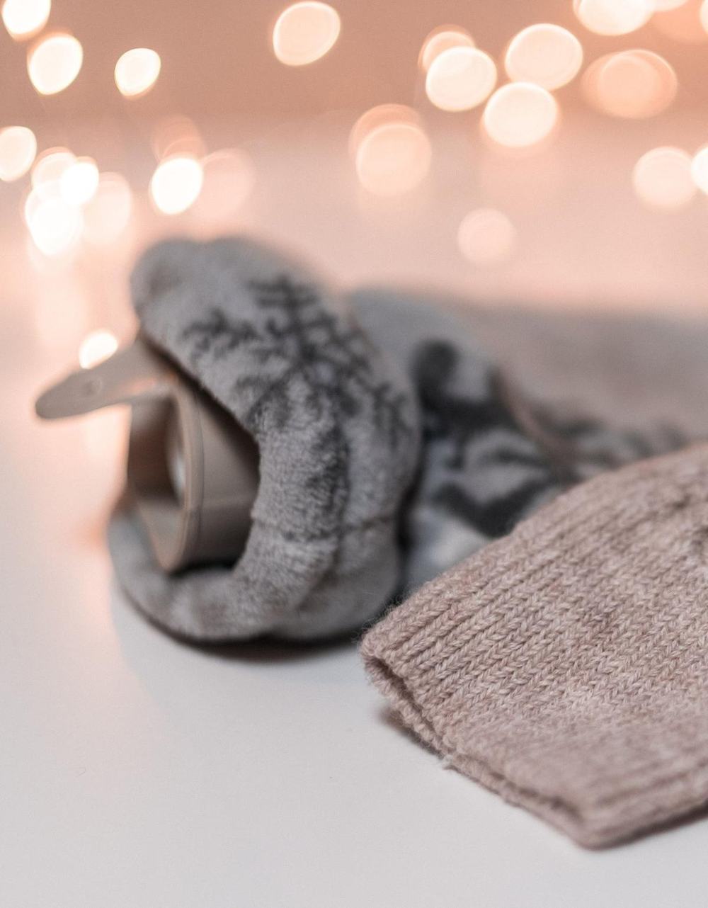 A hot water bottle in a grey knit cover with snowflakes