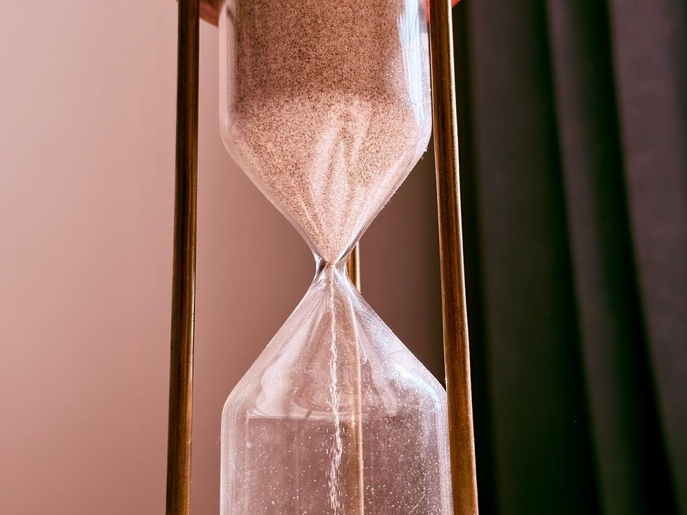 Close-up of fine sand falling through the narrow middle of a wooden hourglass