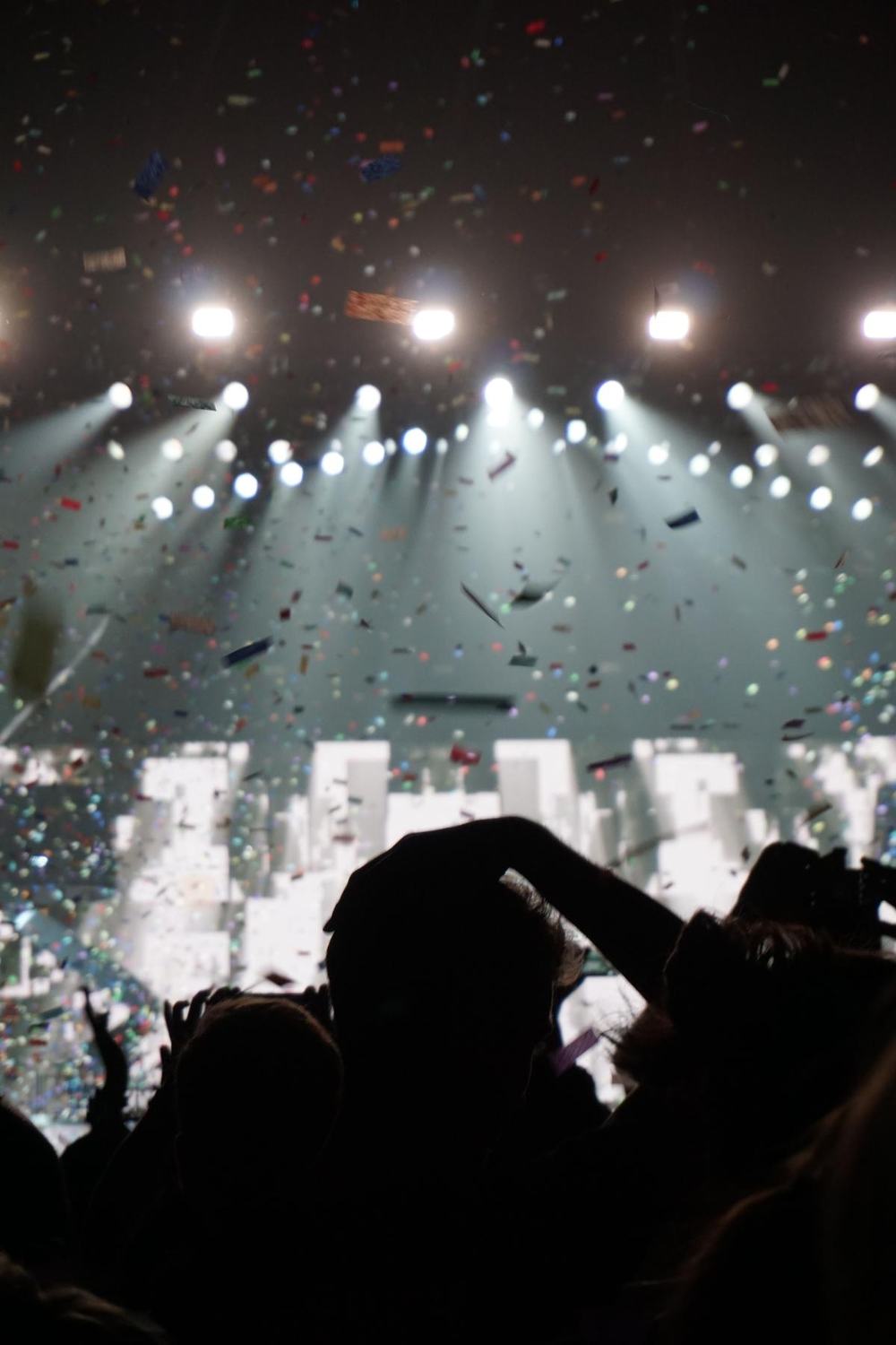Confetti falling over a crowd at a concert, stage lights shining through