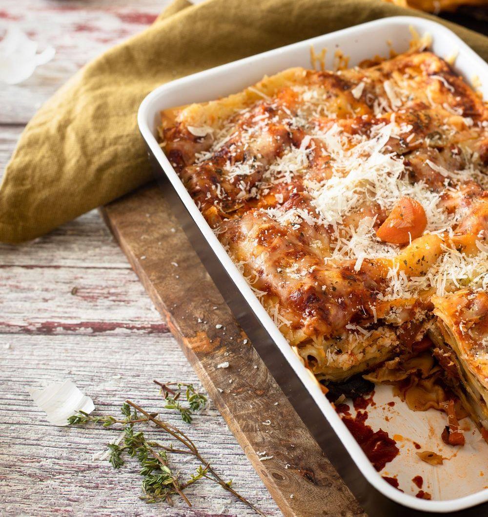 A baked lasagna in a white dish on a wooden board, with one piece already served