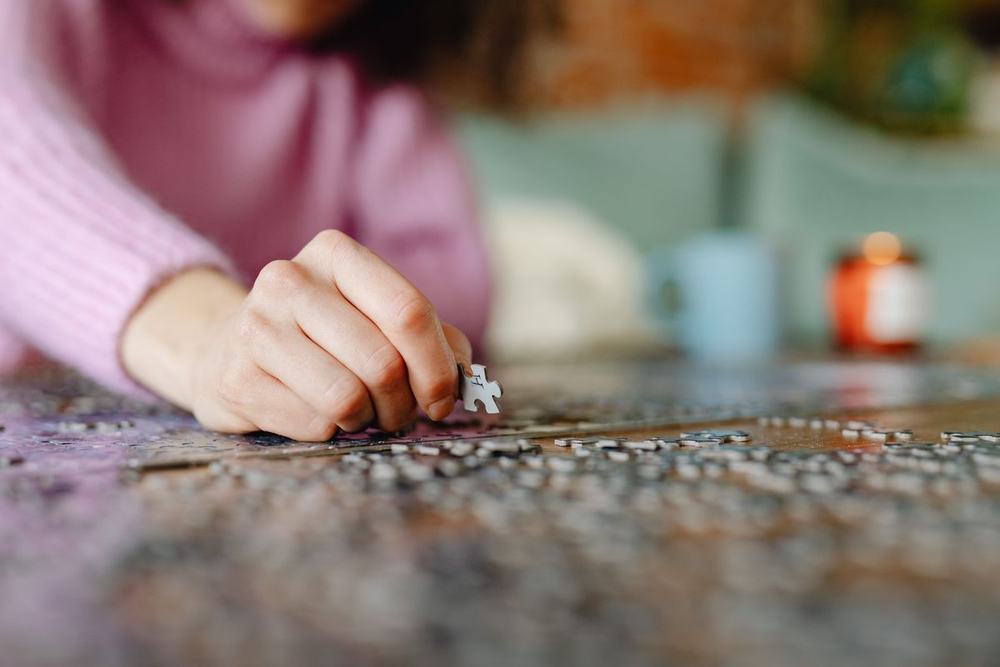 A hand placing a piece into a jigsaw puzzle on a table