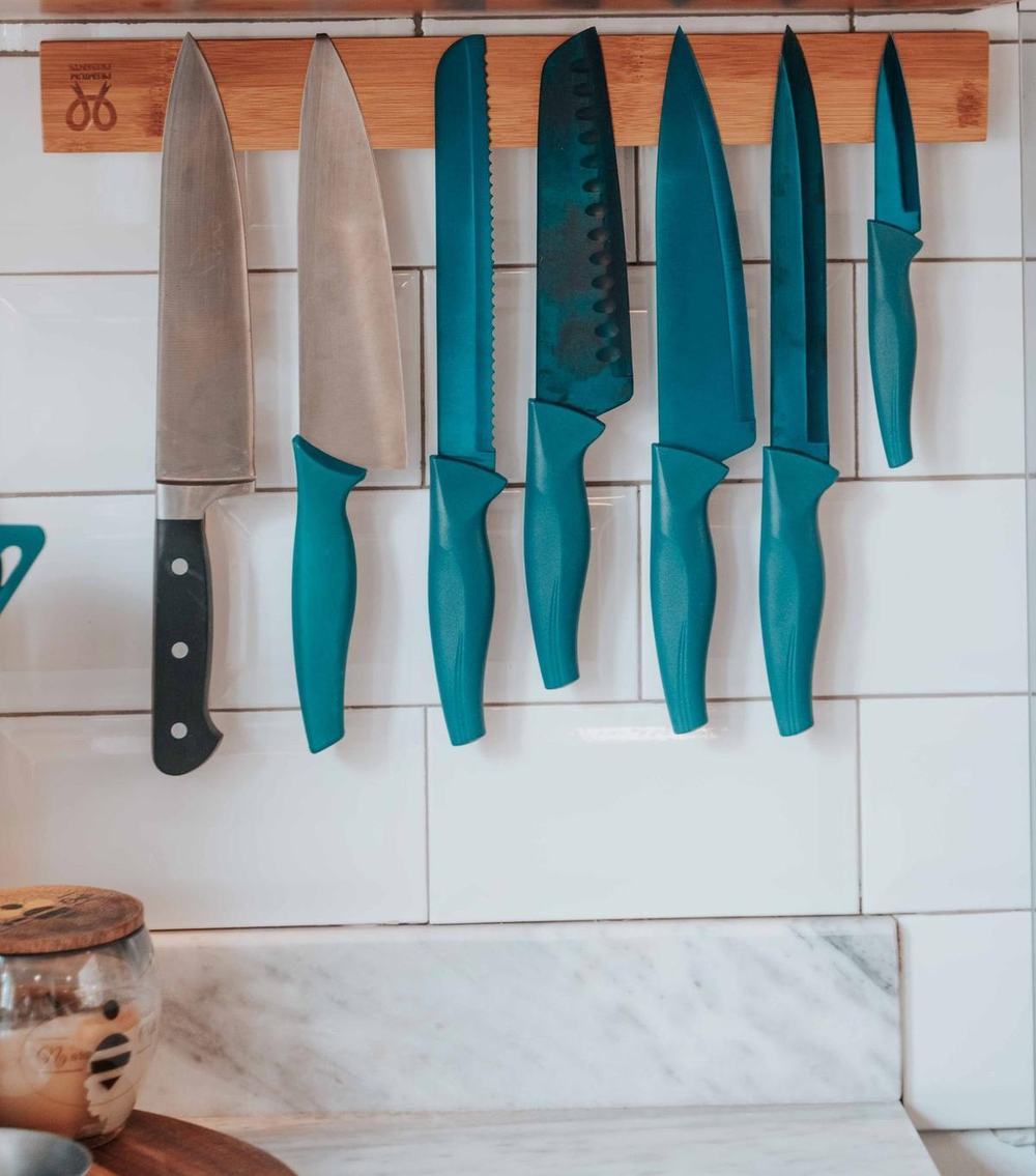 A bamboo magnetic knife strip holding knives on a white tiled kitchen wall