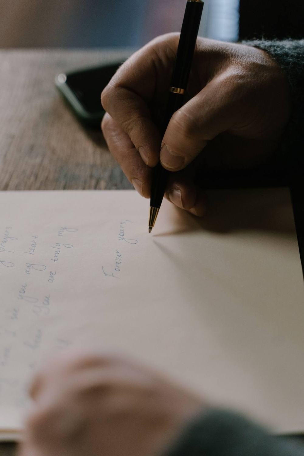 A hand writing a letter in blue ink with a black pen on cream paper