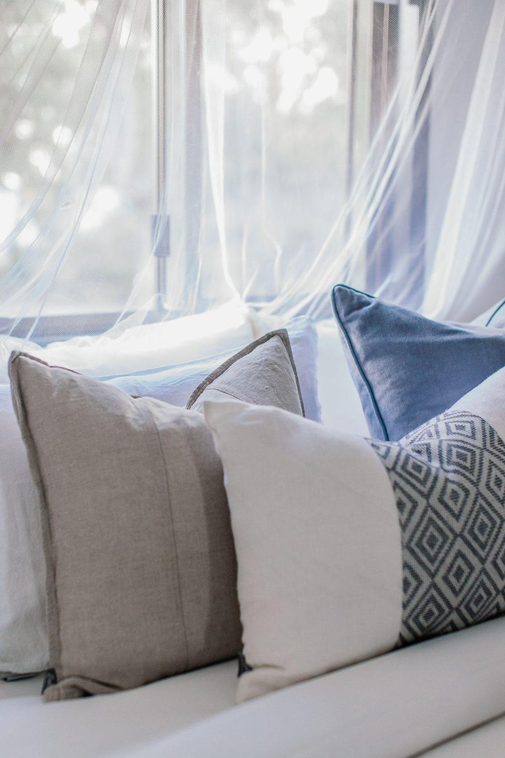 Neutral linen throw pillows in beige, cream and blue on a window seat with sheer curtains