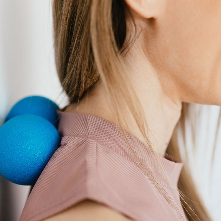 A woman's neck and shoulder resting against a blue massage ball on a white wall
