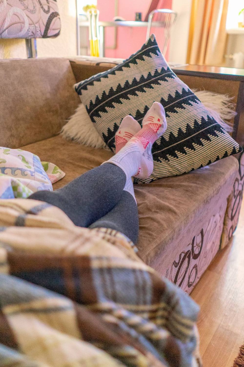 Feet in warm socks resting on a sofa with soft cushions and a plaid blanket