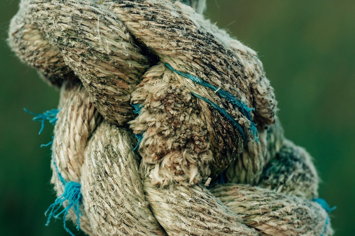 A thick, frayed rope tied in a tight knot against a dark green background