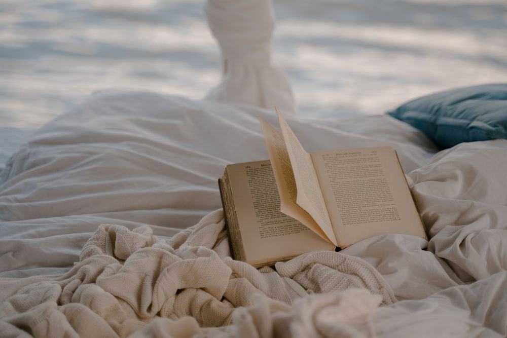 An open book lying on rumpled white bedding