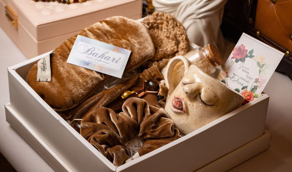 An open gift box with soft velvet scrunchies, a ceramic mug and a small card