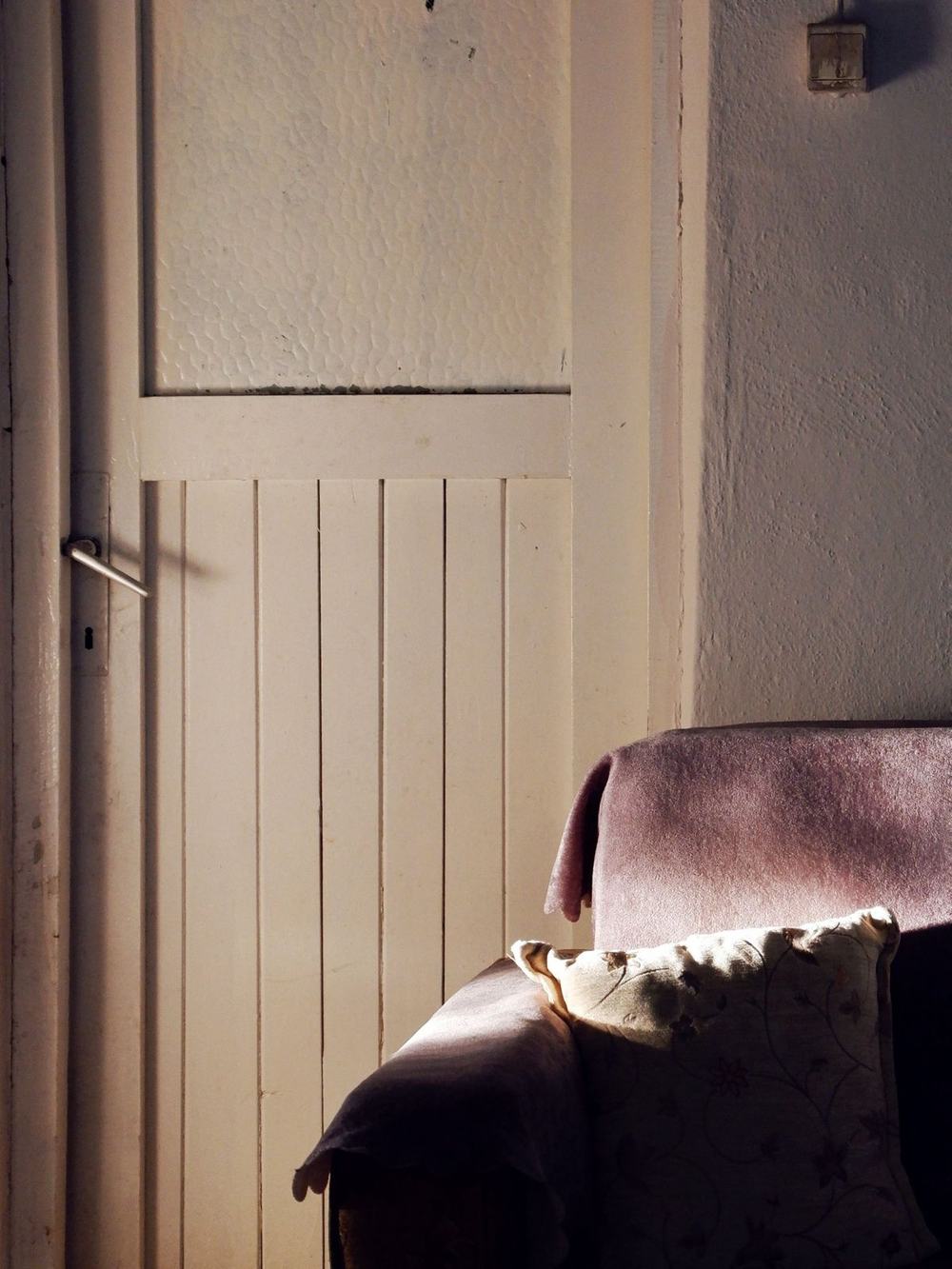 Soft morning light on an armchair with a blanket and a cushion beside a closed white door