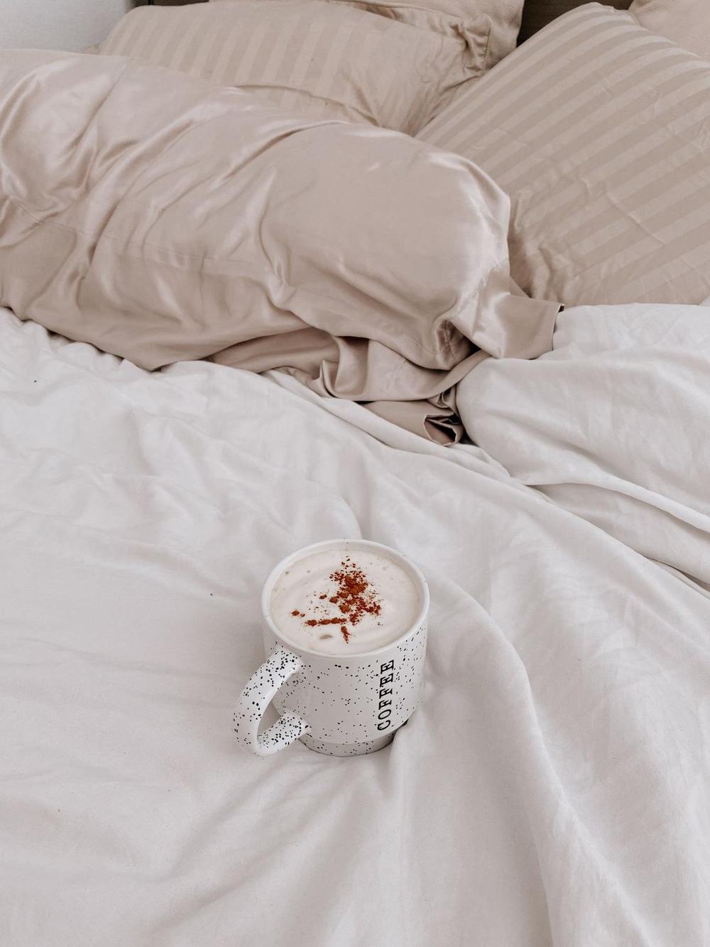 A champagne silk pillowcase on a bed with a cup of cinnamon coffee