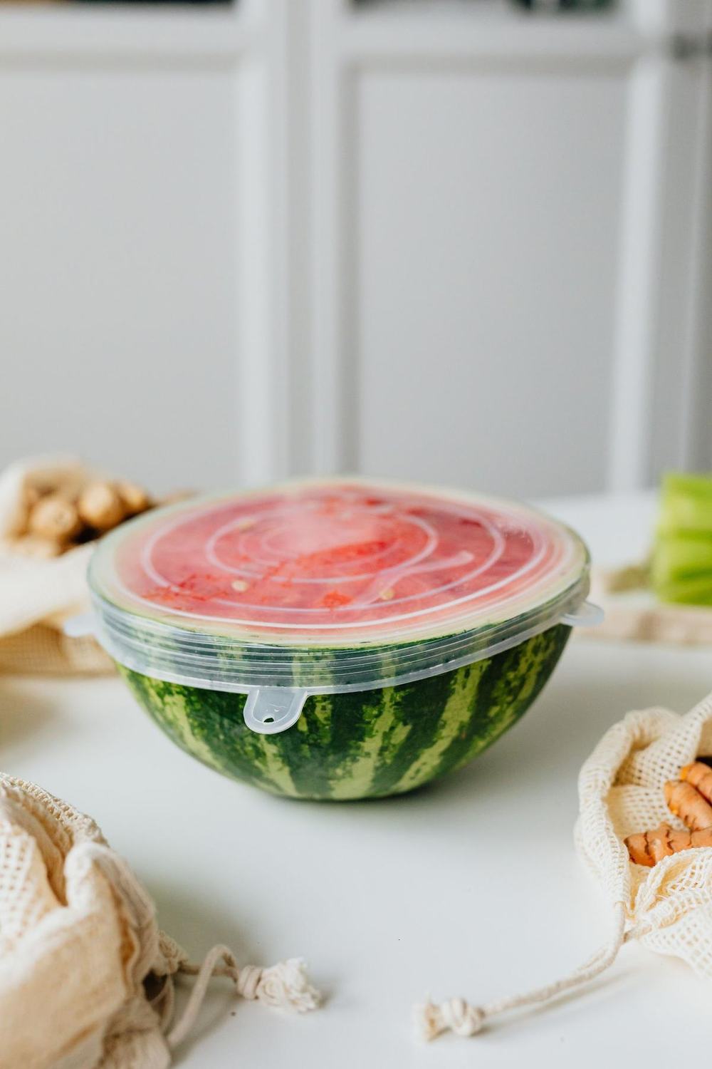 A clear silicone stretch lid sealing a cut half watermelon on a kitchen table