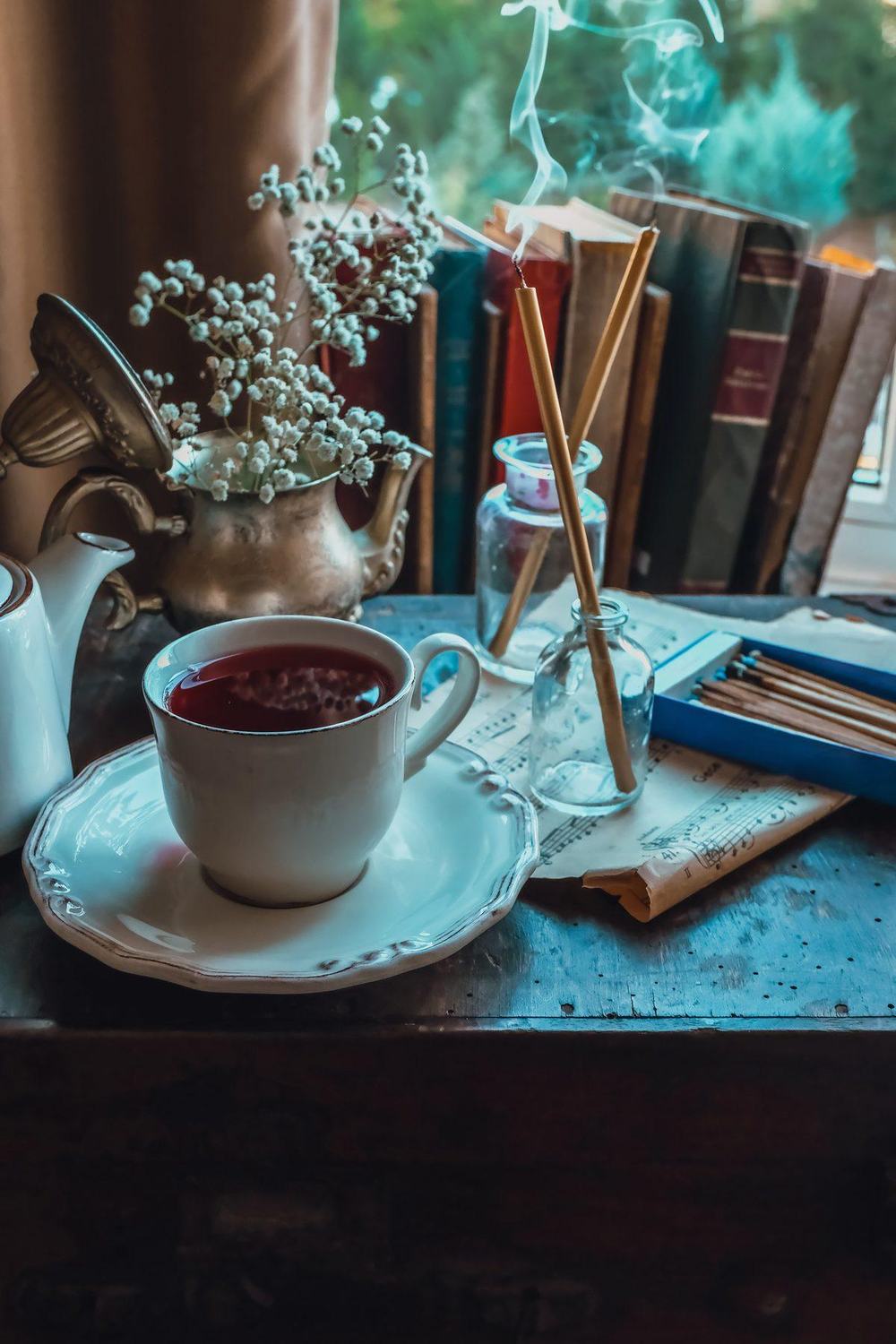 Cup of red tea on a saucer by a window with old books and dried flowers