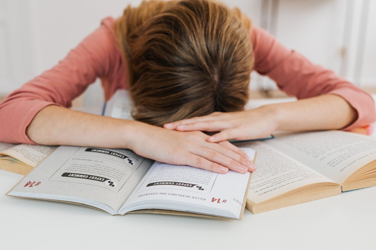 A woman resting her head on her arms over an open book on a white table