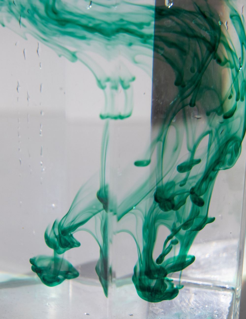 Green ink slowly spreading through clear water in a glass