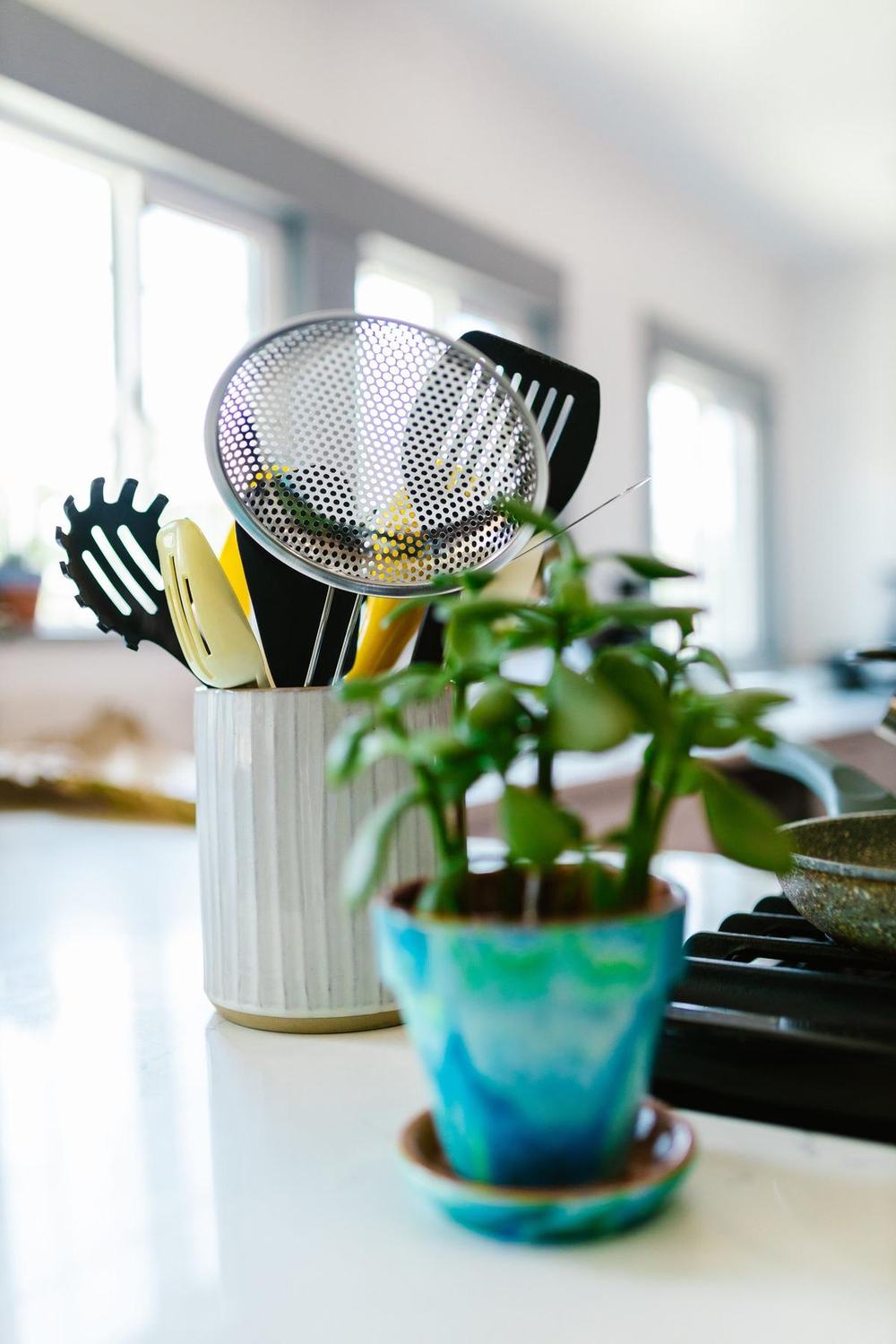 A white ribbed ceramic utensil crock full of kitchen tools on a bright counter