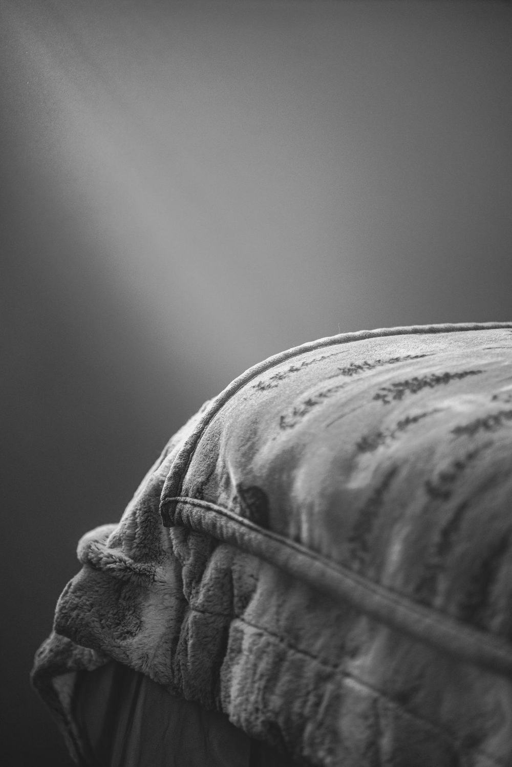 A soft plush weighted blanket draped over a bed in moody black and white light