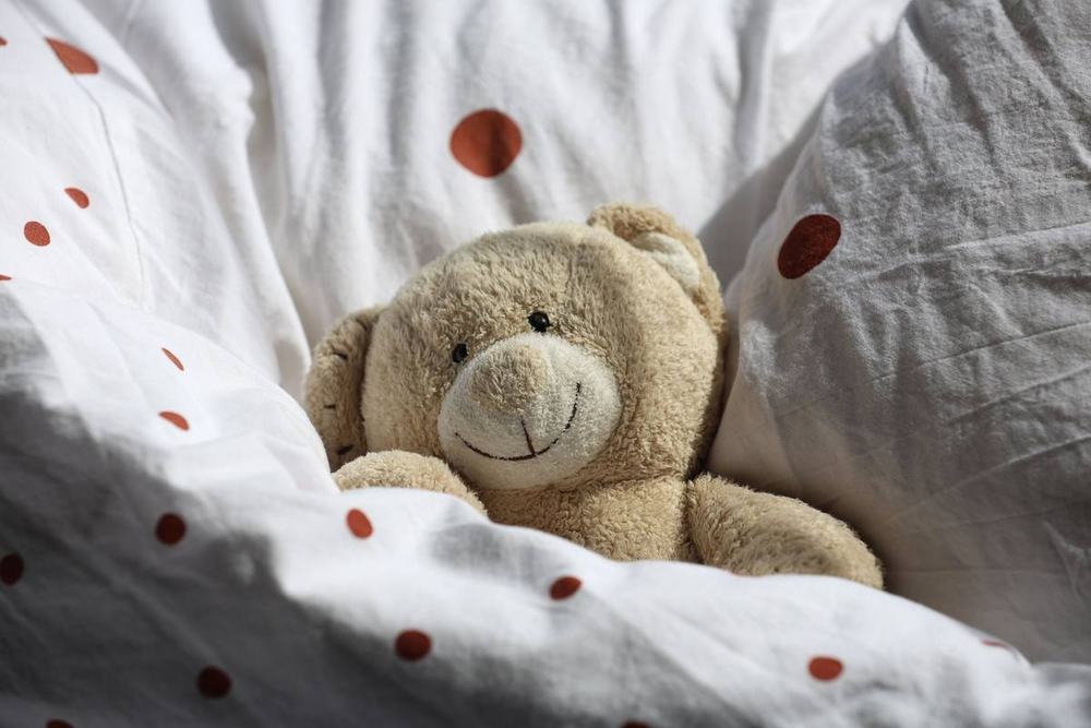 A soft teddy bear tucked into white bedding with red polka dots
