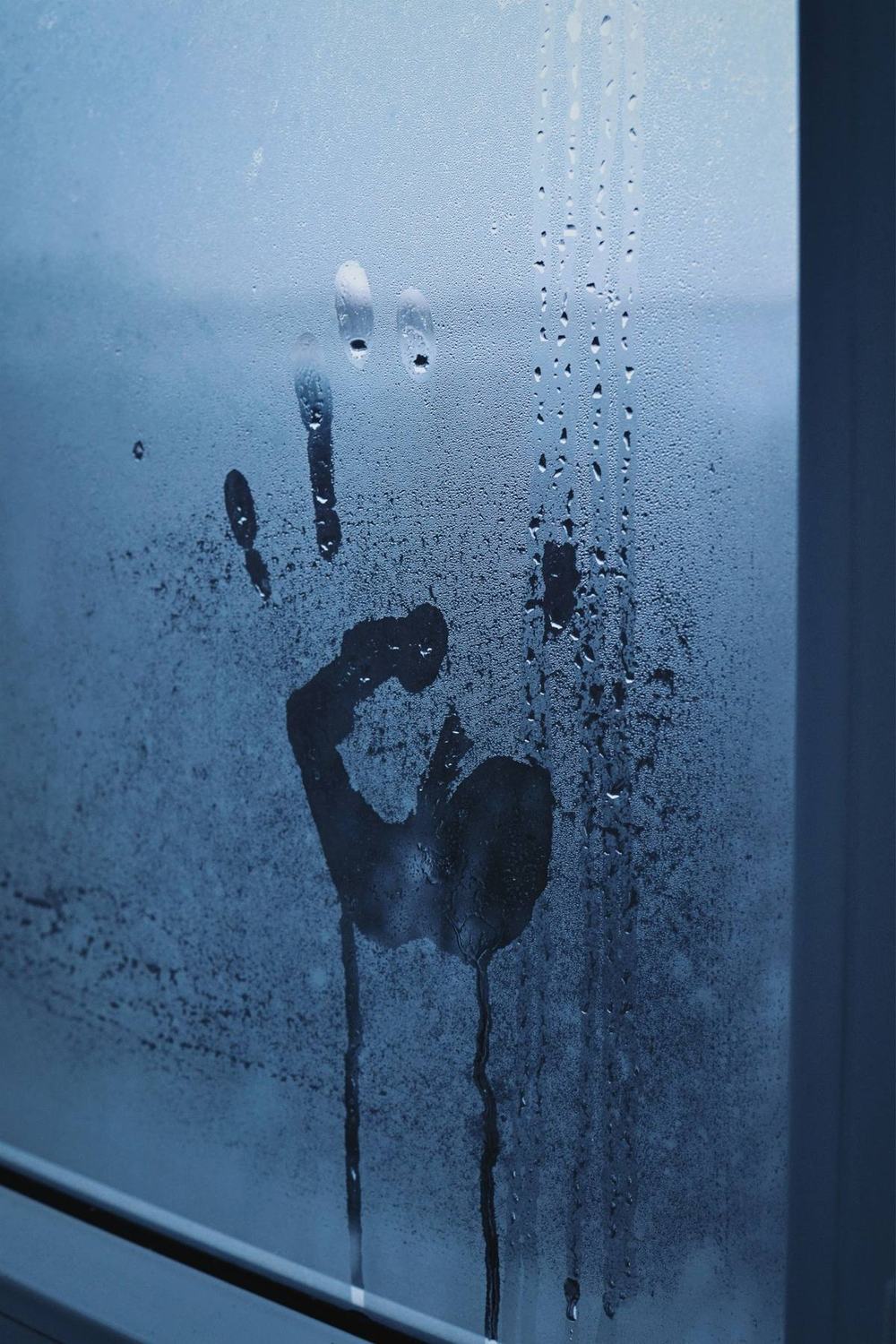 A handprint on a fogged-up window with drops running down the glass