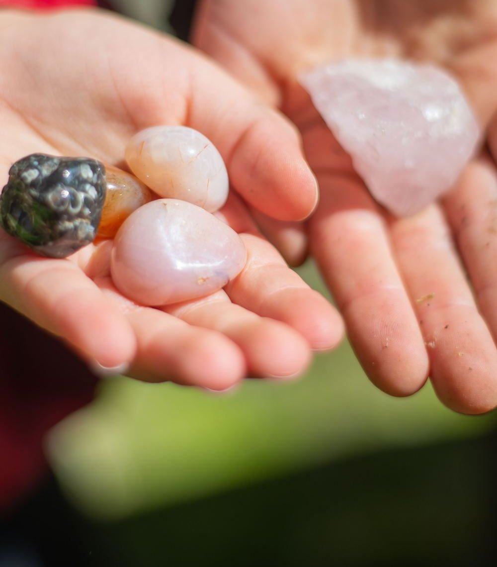 Open hands holding small polished stones and a piece of rose quartz